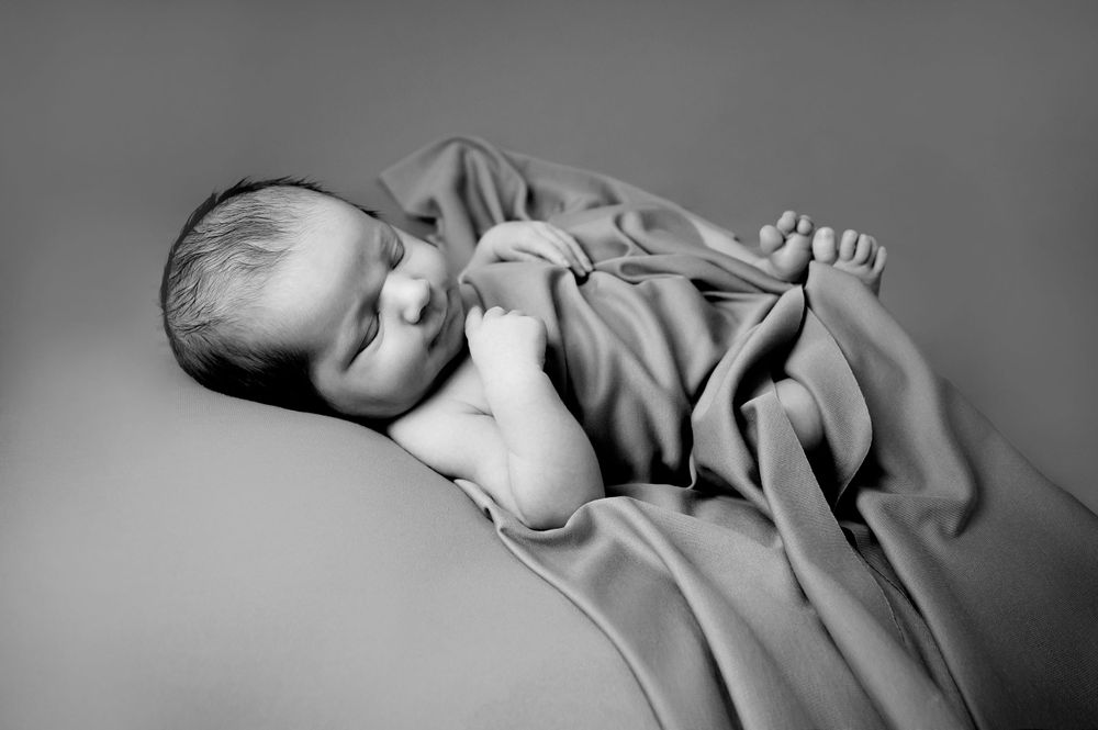 Black and white portrait of a sleeping newborn wrapped in soft grey fabric.