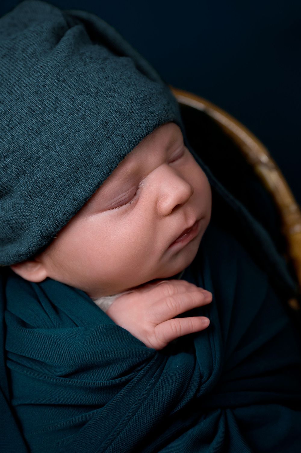 Sleeping newborn wearing teal hat and wrap in close-up portrait.