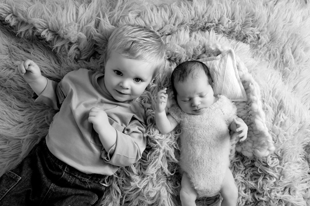 Black and white portrait of siblings lying together on soft textured rug.