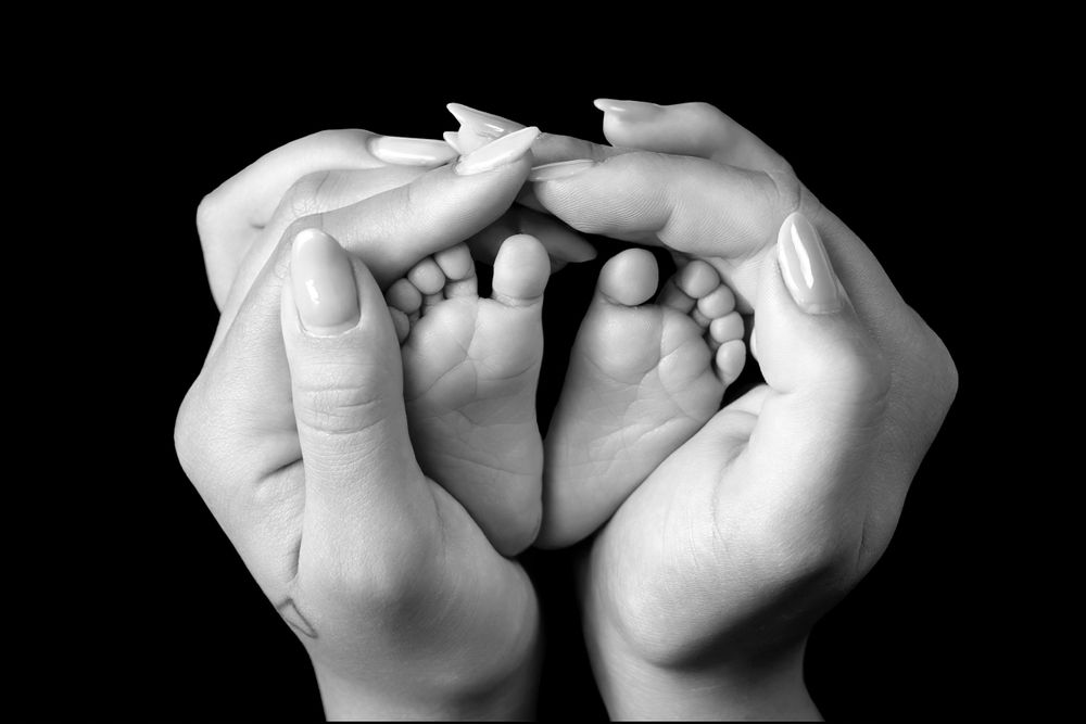Black and white image of small baby feet cradled in adult hands.