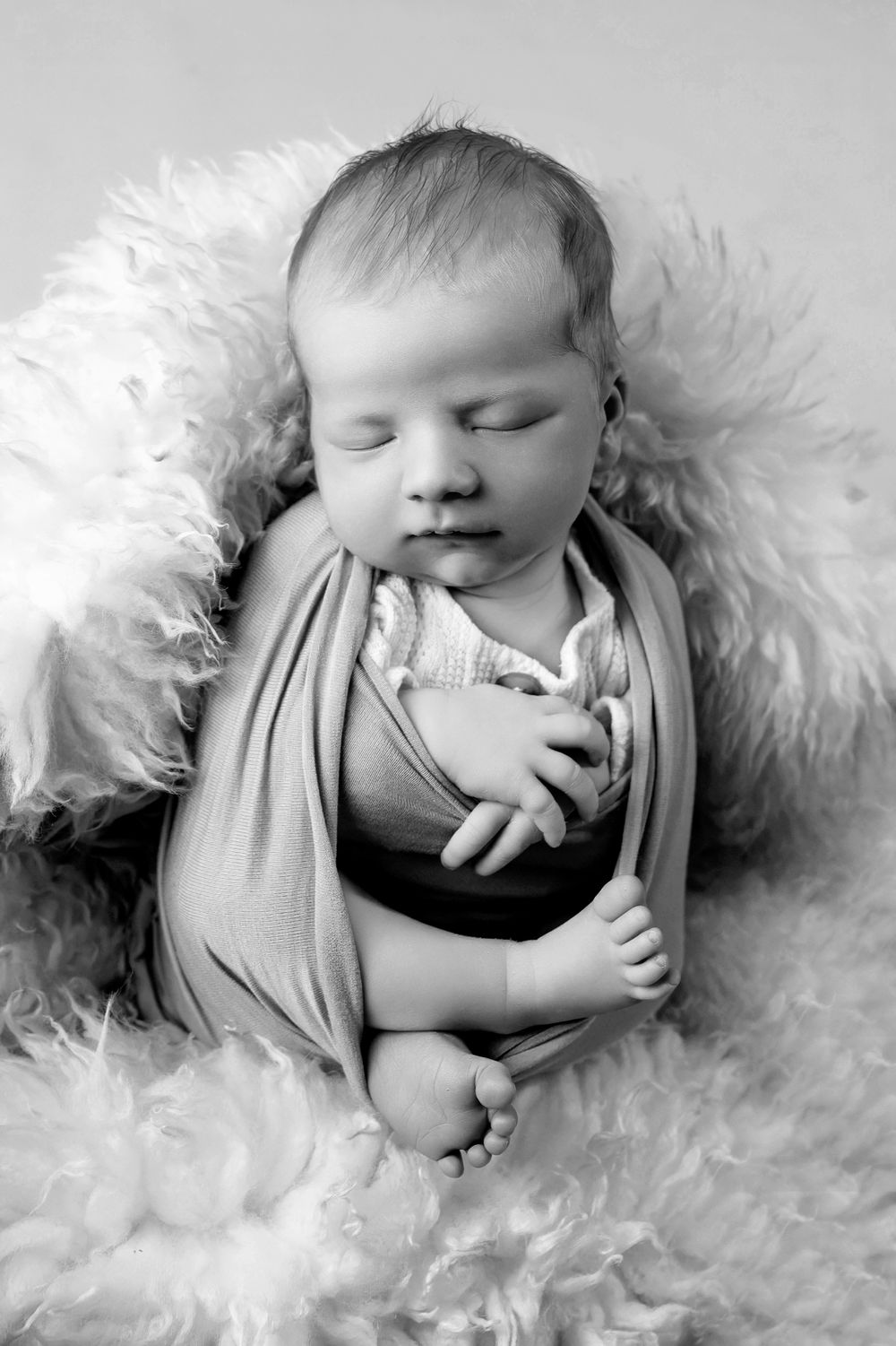 Black and white portrait of sleeping newborn wrapped in fabric on fluffy white background.