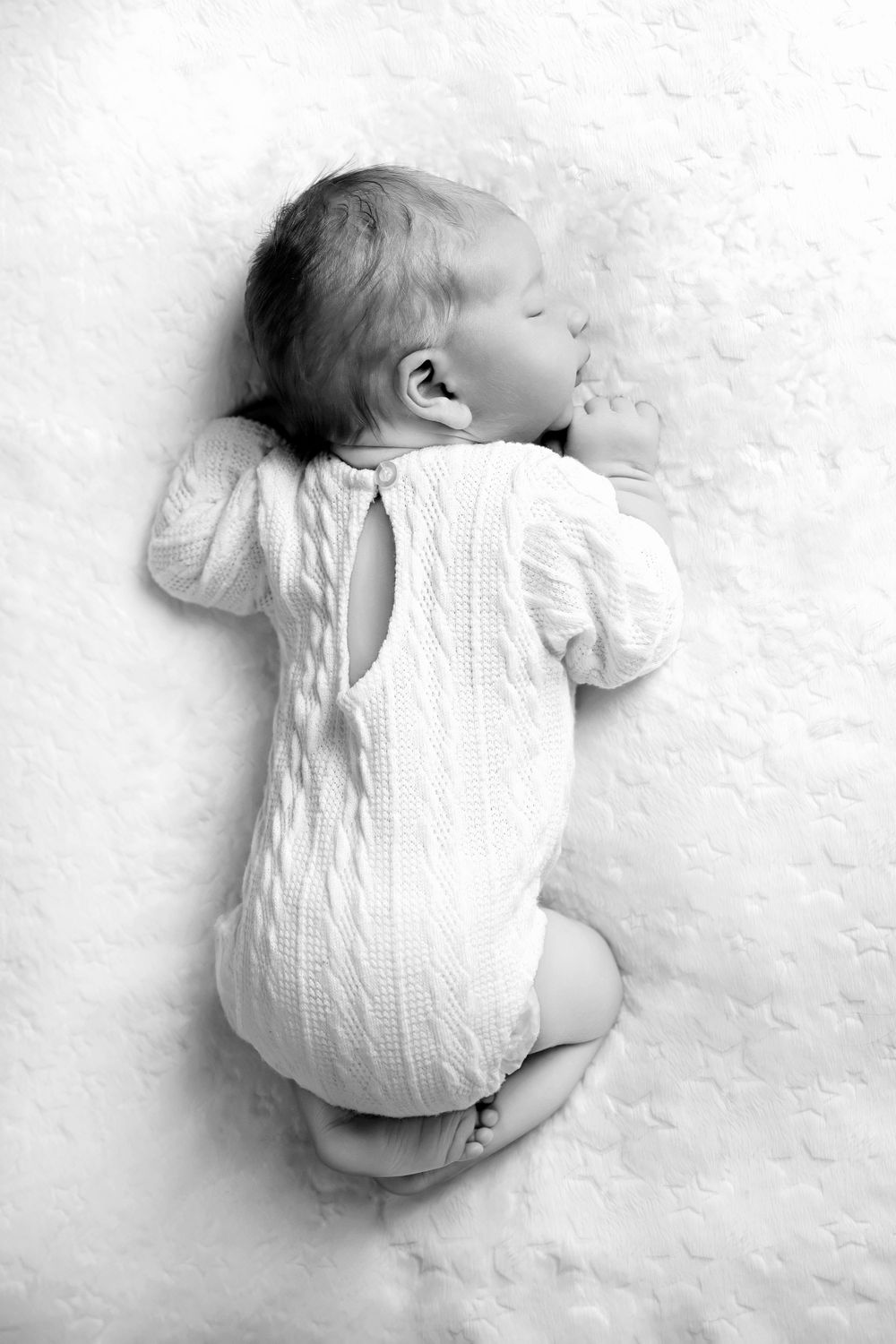 Black and white image of newborn in cable-knit outfit lying on textured surface.