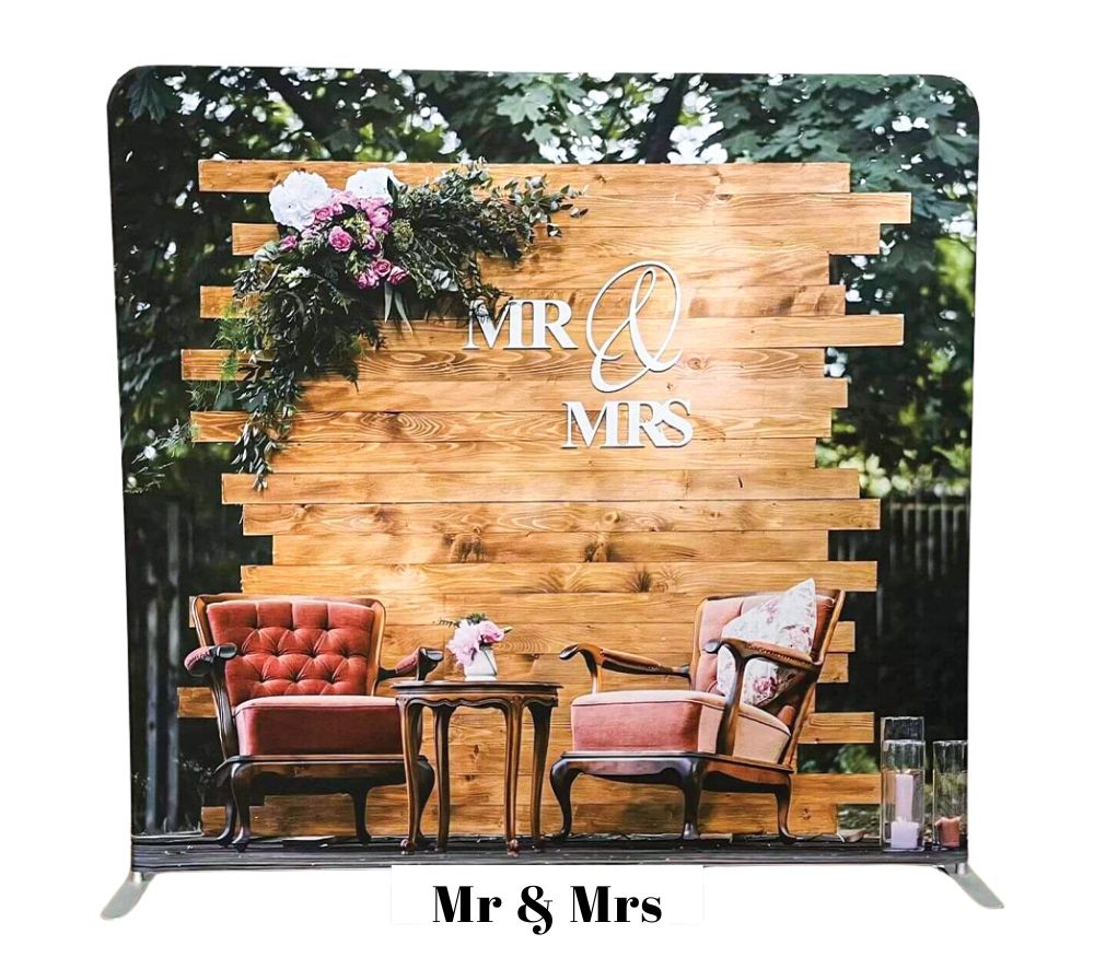 Rustic wooden backdrop with 'Mr & Mrs' sign, vintage furniture and floral decorations for wedding photo booth setup.