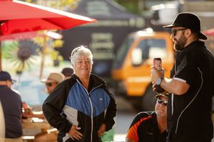 Two people having a conversation outdoors at a casual gathering with one person wearing a black jacket and cap.