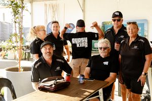 A group of casual friends gathered around a table outdoors at a venue wearing black shirts.