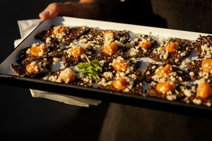 Appetizing platter of dark sushi rolls garnished with orange tobiko, sesame seeds and microgreens on a black plate.