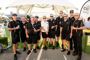 A team in matching black uniforms poses together under a white tent at an outdoor event.