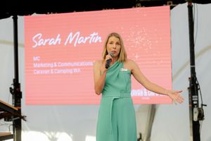 A presenter in a mint green outfit speaks on stage with a pink presentation screen behind her.