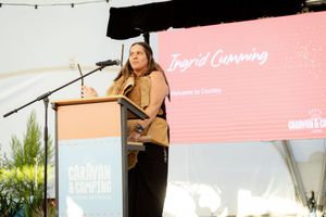 Speaker presents at an outdoor event with a pink backdrop displaying text.