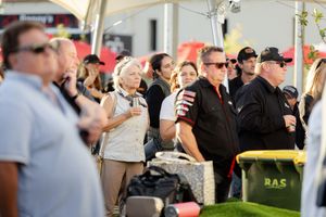 An engaged crowd watches attentively during an outdoor tent event on a sunny day.
