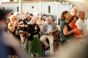 A crowd of people sitting and laughing at an outdoor event as they enjoy a celebration together.