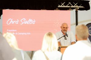 A speaker presents at a podium with a pink digital display showing text in the background.
