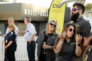 Group of people enjoying drinks and conversation at an outdoor event with black attire and sunglasses.