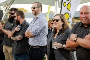 Group of casually dressed people standing outdoors at an event wearing sunglasses and smiling.