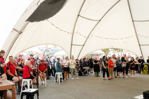 Large crowd gathered inside a white tent structure during a social event with string lights overhead.