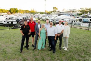 A group posing together on grass with boats and marina in the background during golden hour.