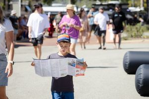 Child reading a map or brochure while attending an outdoor event on a sunny day.
