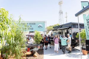 Food trucks and customers gather at an outdoor market with a tropical Bandit River Market sign visible.