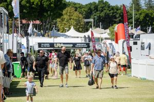 Crowds walk through vendor booths and tents at an outdoor festival on a sunny summer day.