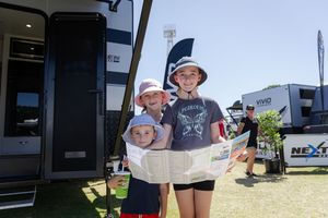 A group stands together in front of an RV at an outdoor event on a sunny day.