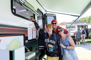 People gathered around recreational vehicle display at outdoor event.