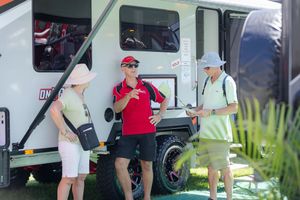 Group chatting next to recreational vehicle at outdoor event in casual summer attire.