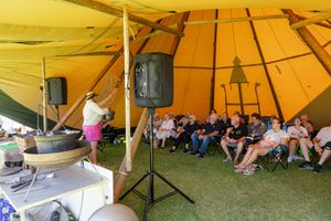 Audience seated under large yellow tent during outdoor presentation.