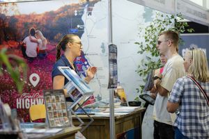 Customers interact with vendor at outdoor market booth with floral backdrop.
