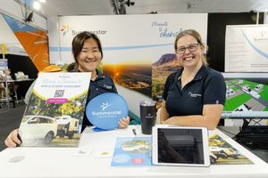 Two friendly staff members at an information booth display promotional materials including brochures and a blue frisbee.