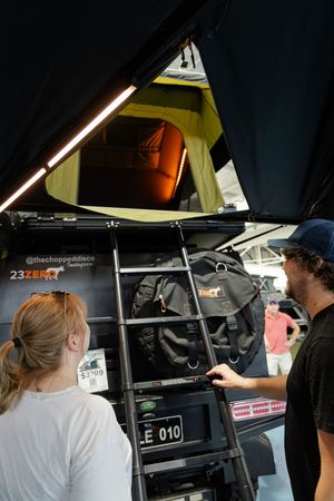 Two people inspecting equipment inside a camping roof tent with lighting installed.