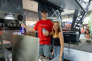 Food service workers in uniform stand at a counter inside a mobile kitchen trailer.