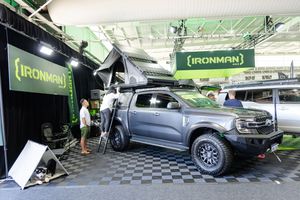 Silver pickup truck parked at IronMan vendor booth display under green tent at trade show.