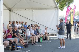 Speaker presenting to seated audience under white event tent.
