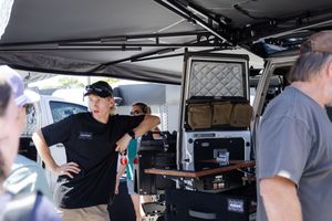 Behind the scenes view of production equipment and crew members gathered near a van during an outdoor shoot.