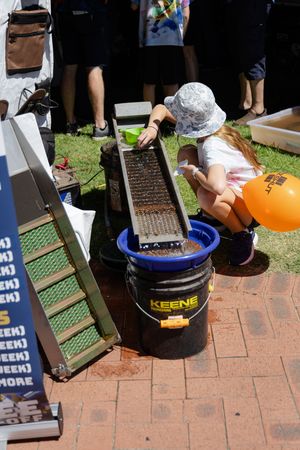 Person in white hat using a gold panning sluice box setup with Keene bucket on brick patio surface.