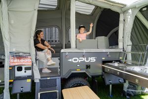 Two people enjoying time together inside a spacious popup camper trailer with storage and camping gear.