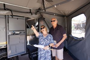 Two people share a cheerful moment inside a vehicle camping setup with grey interior walls.