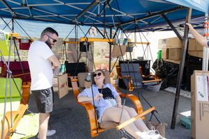 Production crew members setting up under a blue canopy tent with equipment and folding chairs visible.