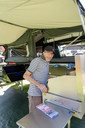A guest stands under an outdoor tent canopy next to a display table.