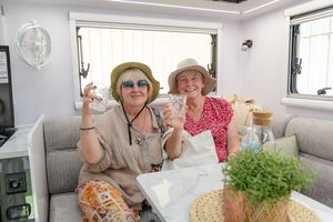 Two people relaxing and enjoying beverages inside a bright recreational vehicle interior with sunlight coming through windows.
