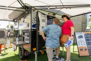 Customers examine an outdoor adventure trailer setup at a camping equipment showcase event.