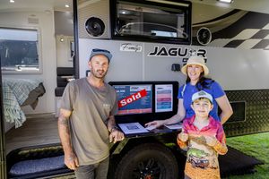 People pose beside a Jaguar branded camper vehicle with interior display screens visible.