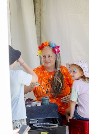 Someone wearing an orange tie-dye shirt and floral crown sits at a table with others during an outdoor gathering.