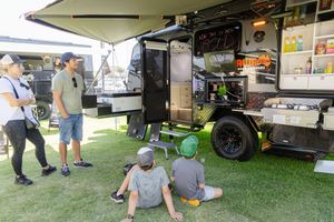 A mobile food truck setup with customers gathering around on grass at an outdoor event.