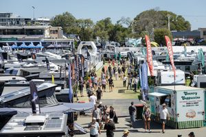 Aerial view of a bustling boat show with crowds walking between rows of yachts and vendor displays on a sunny day.