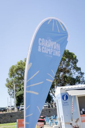 A blue teardrop-shaped promotional banner for caravan and camping against a clear sky with trees in background.