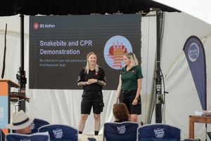 Two instructors demonstrate CPR and snakebite first aid procedures on stage at a workshop.