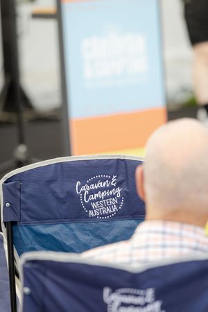 Close-up of a navy blue camping chair with cursive logo text at an outdoor event.