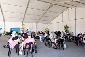 A large white event tent filled with attendees seated at round tables during a conference.