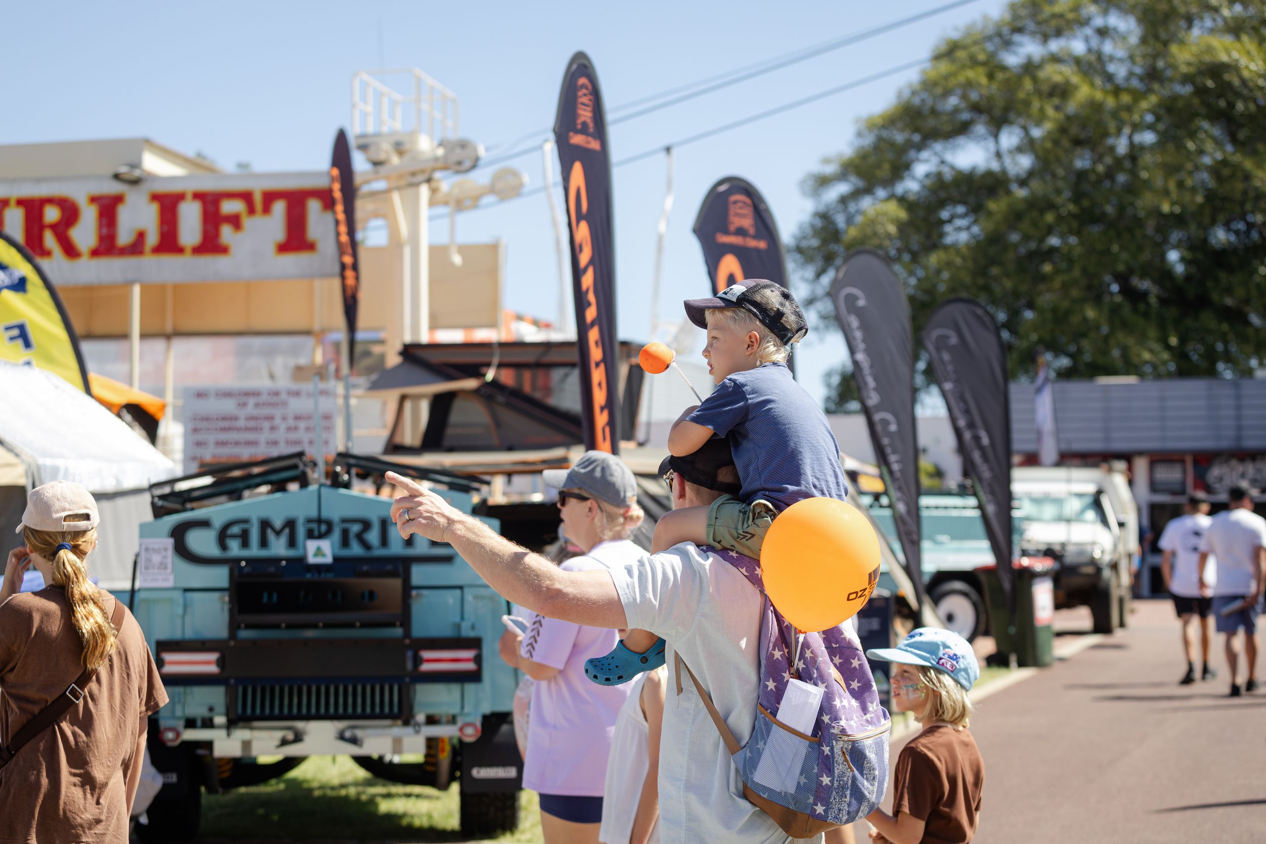Visitors enjoying a sunny day at an outdoor festival with balloons and display banners.